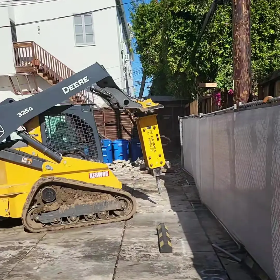 Skid steer breaking up concrete to prepare a backyard lot for construction