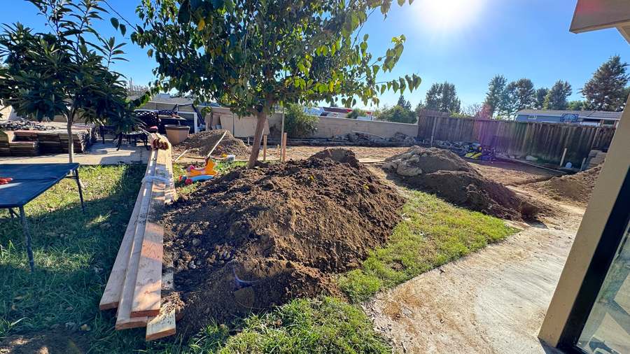 Backyard site prep for an ADU: excavated soil, lumber stack and lawn