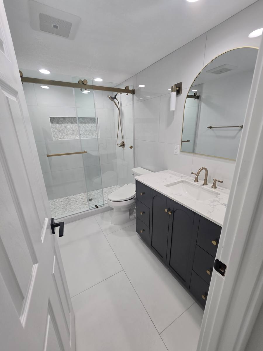 Remodeled bathroom with glass shower enclosure, navy vanity and white tile