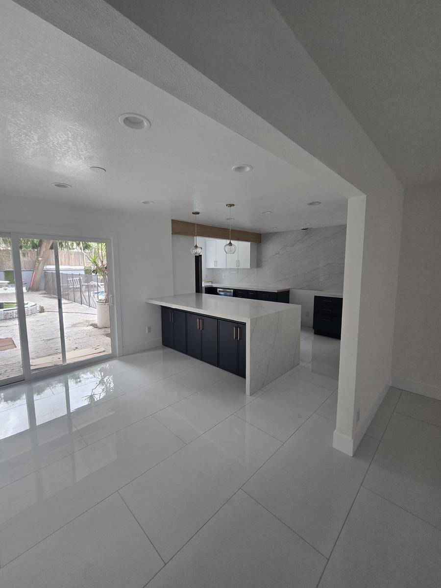 Open-plan remodel: navy kitchen island and cabinets, large white floor tile, sliding door to the yard