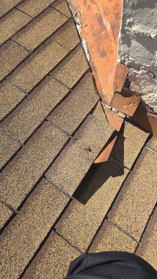 Roof inspection close-up: rusted, lifted flashing at the base of a chimney